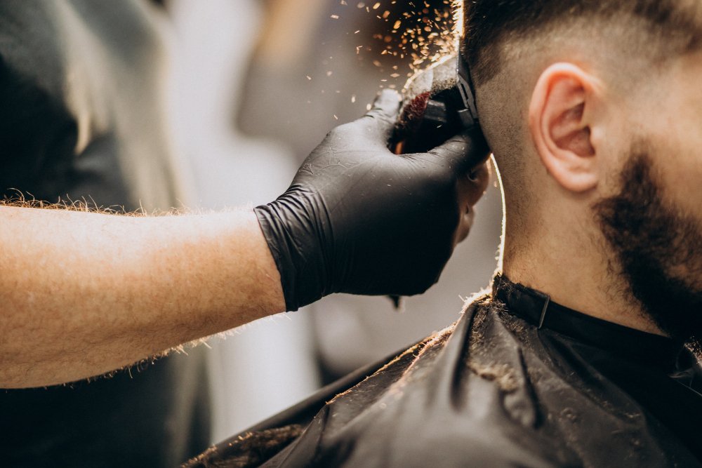 Barber w czarnej rękawiczce wykonuje cieniowanie włosów (fade) maszynką u klienta w salonie.